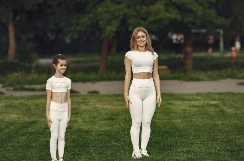 A woman and girl in white activewear standing on a grass field outdoors, smiling.